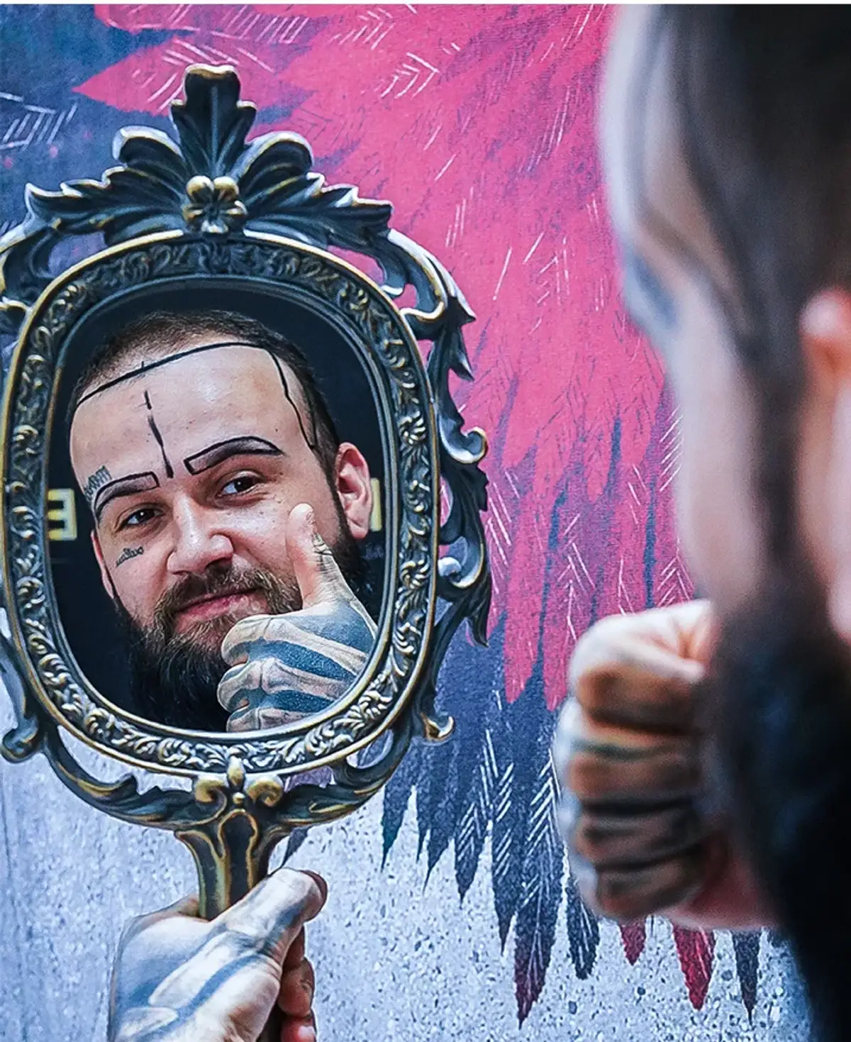 An unidentified patient holding an ornate hand mirror up to his own face after a session, the newly placed grafts visible along the front hairline.