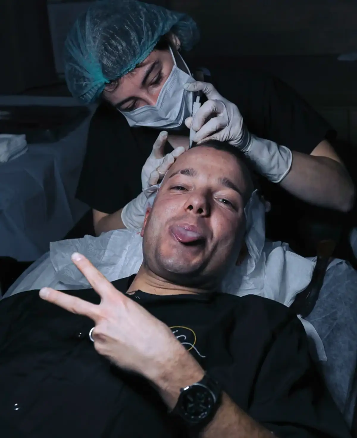 Two clinicians in caps and masks working over an unidentified patient reclined in a treatment chair during a session.