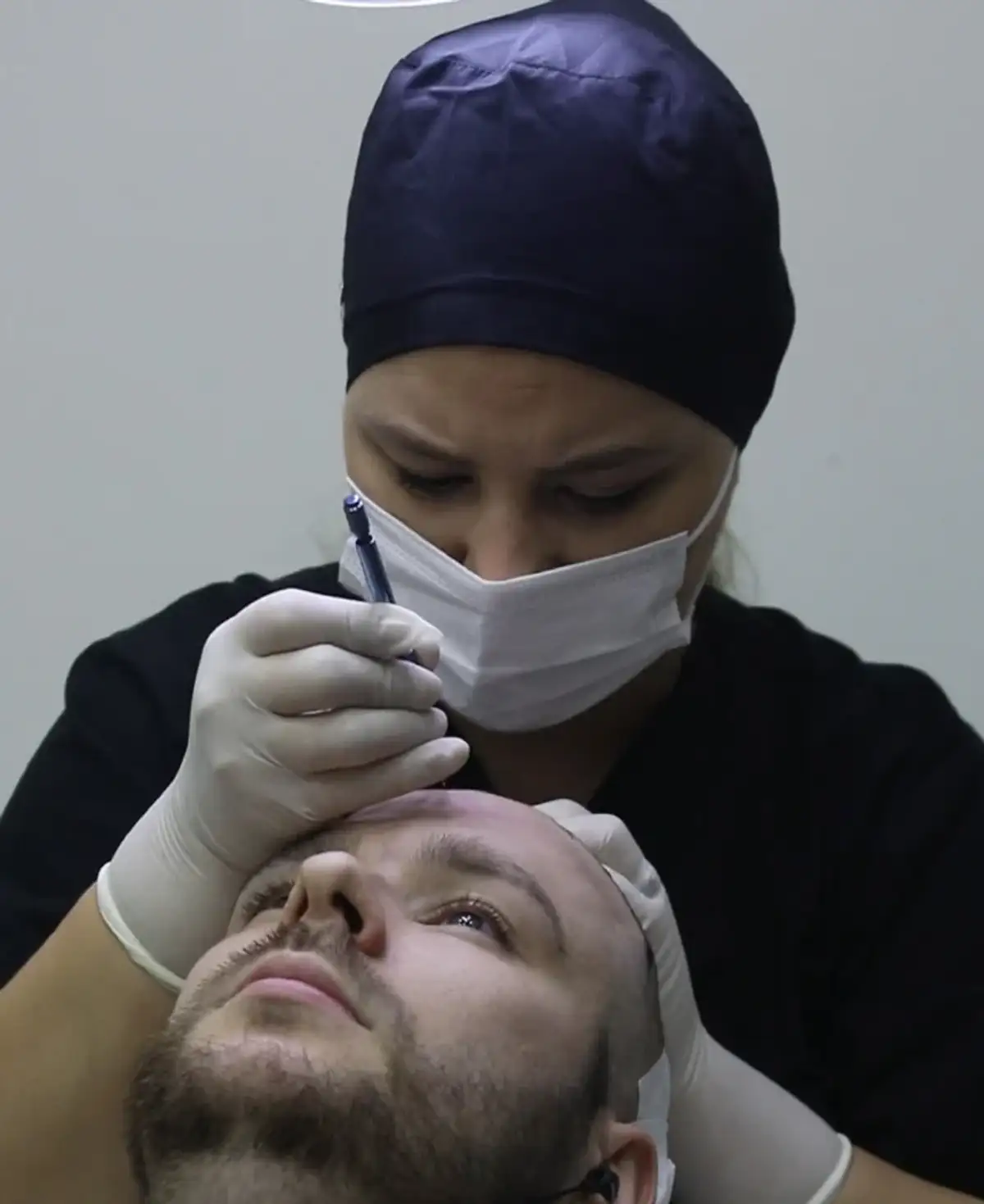 Un clínico con gorro y mascarilla quirúrgicos trabajando sobre la frente de un paciente no identificado reclinado en una silla de tratamiento.