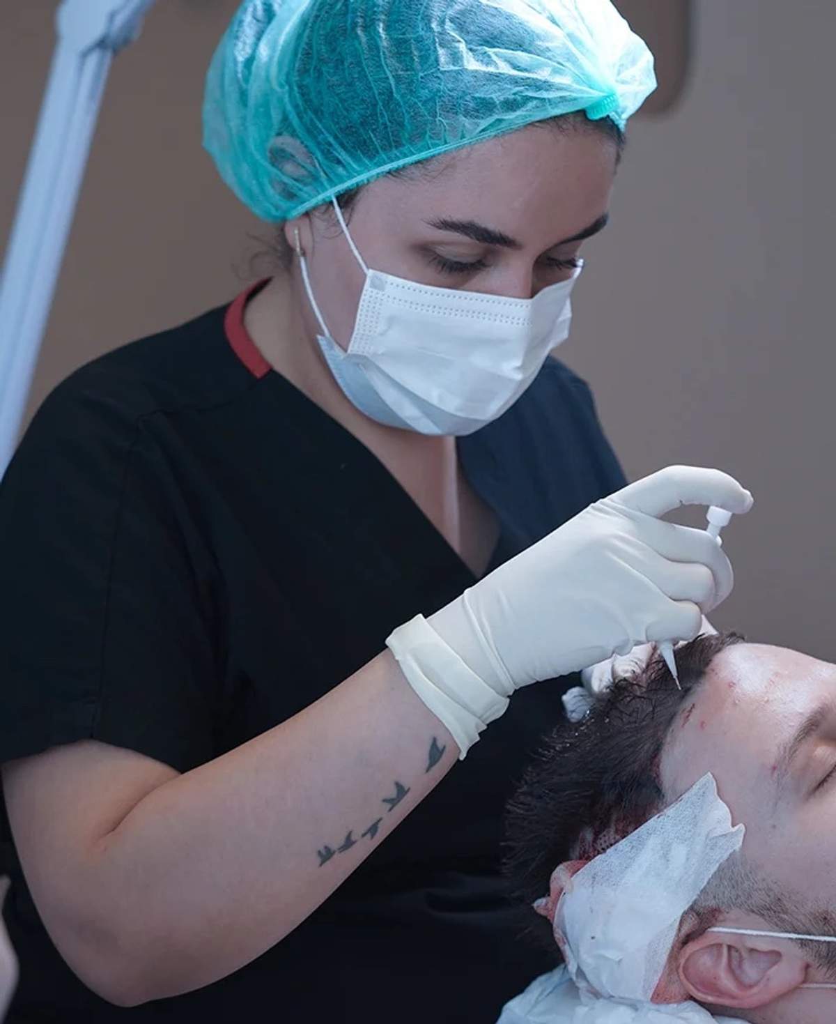 A gloved clinician in a surgical cap working along a patient’s front hairline in a treatment chair