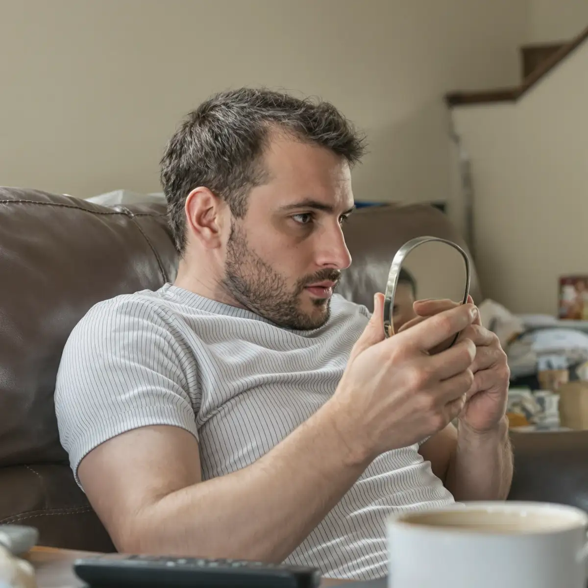 Man examining his hairline in a hand mirror to check how his hair transplant results are holding up