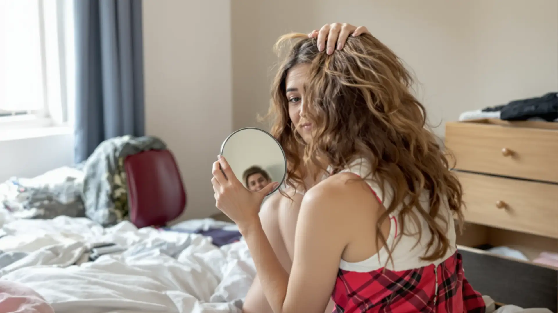 Woman lifting the hair at her hairline with a hand mirror to check a high forehead.
