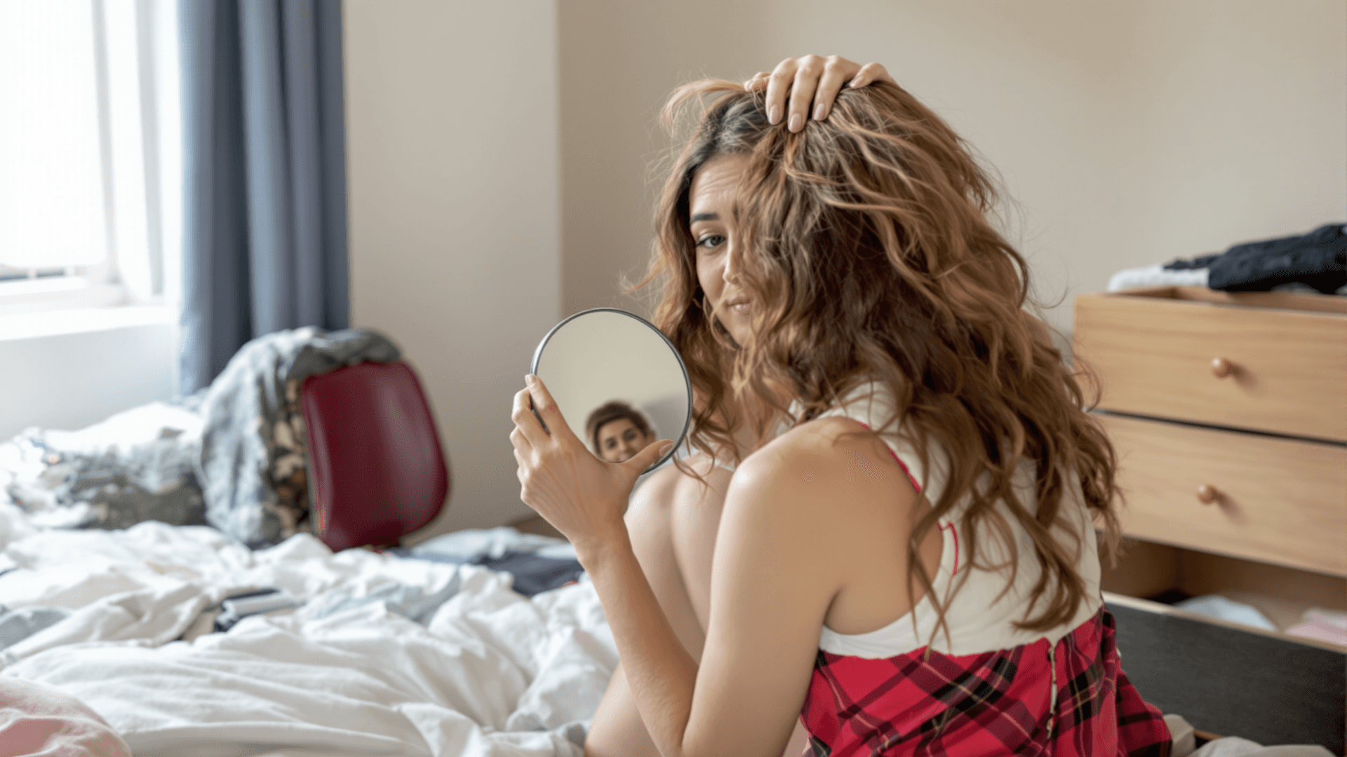 Woman lifting the hair at her hairline with a hand mirror to check a high forehead.