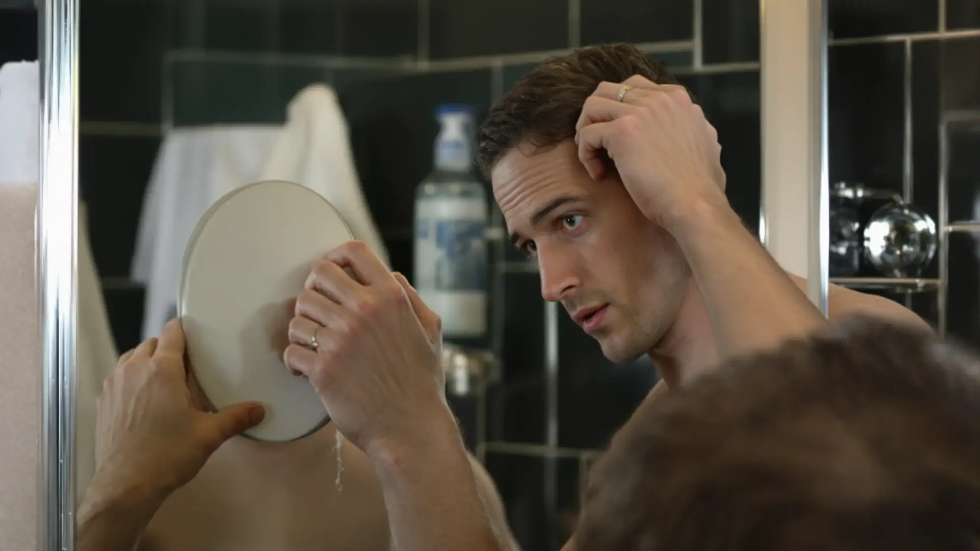 Man inspecting a thinning hairline in a bathroom mirror at home