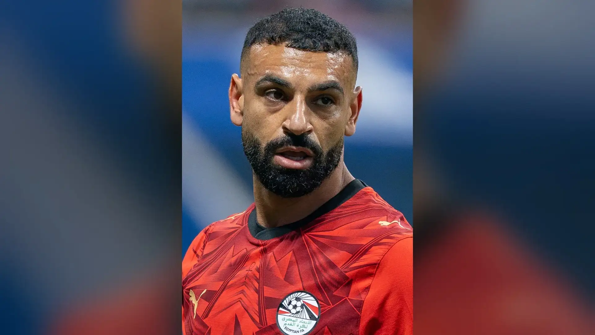 محمد صلاح بقميص منتخب مصر الأحمر على أرض الملعب، مصوّر من الأمام وشعره المجعد وصدغاه ظاهران.
