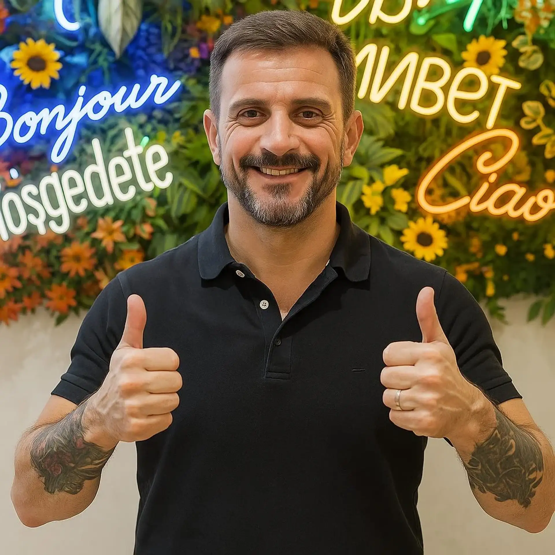 Smiling man giving a thumbs up in front of a colorful floral wall with welcoming signs.