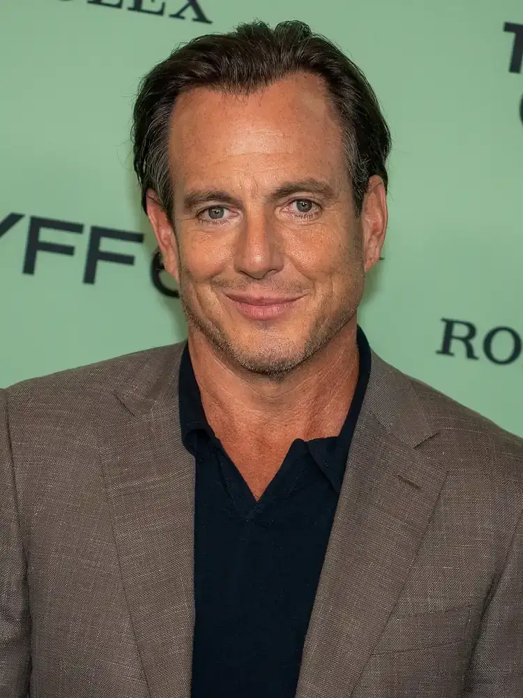 Will Arnett at a 2025 film premiere in a tan jacket, photographed front-on under press lighting with his hair combed back off the forehead.