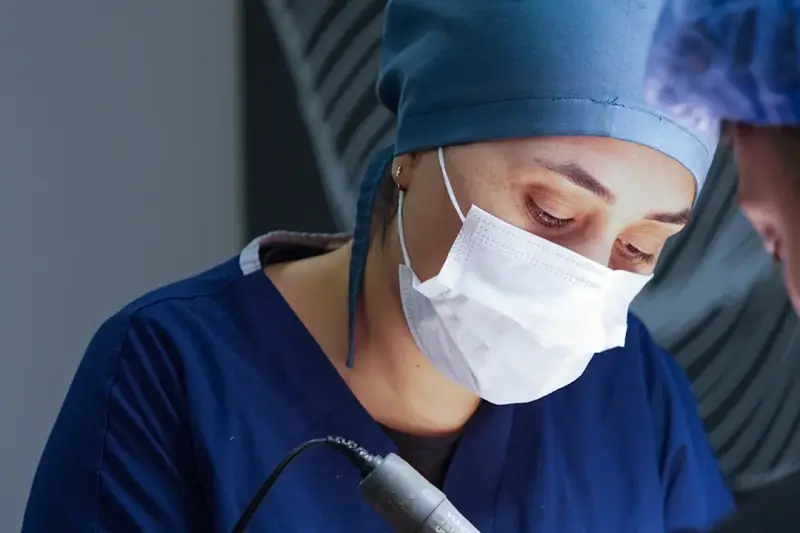 Doctor in a surgical cap and mask working with a handheld instrument during a hair transplant