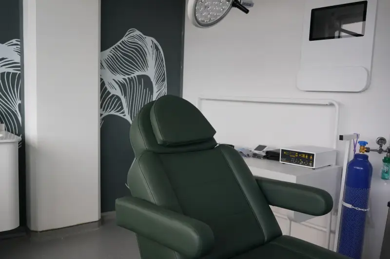 Green treatment chair beside a work table with an electronic device, an oxygen cylinder and a surgical light above