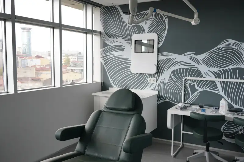 Operating room with a green reclining chair, surgical lights, a work table and windows facing the city