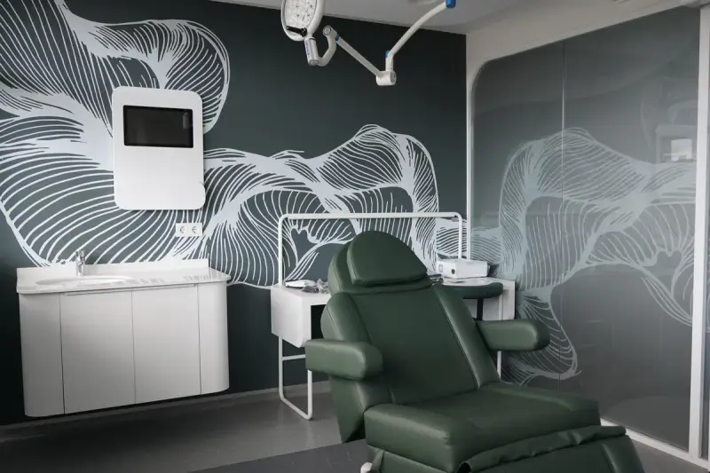 Green reclining chair in an operating room with a surgical light, wall screen, washbasin and glass partition