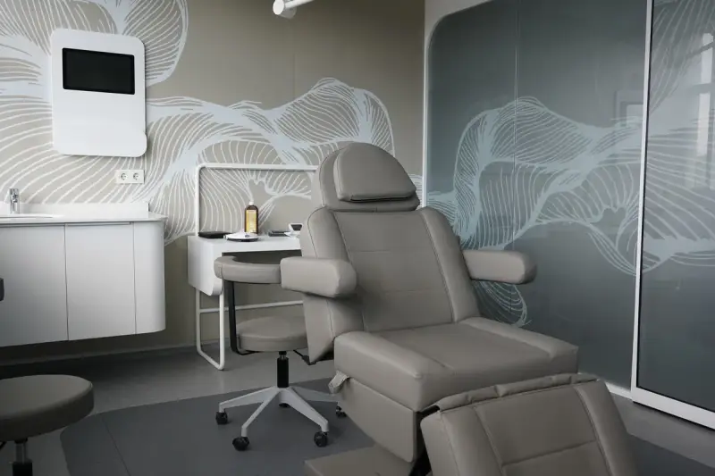 Operating room with a grey reclining chair, a stool, a washbasin and a frosted glass partition