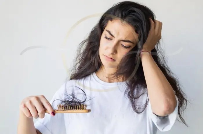 Woman noticing shed hair on her brush during hair loss recovery