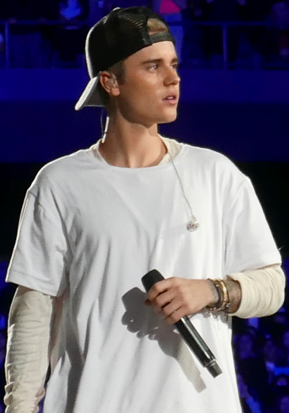 Justin Bieber performing on stage in a backwards baseball cap, the cap covering his forehead so that no hairline is visible.