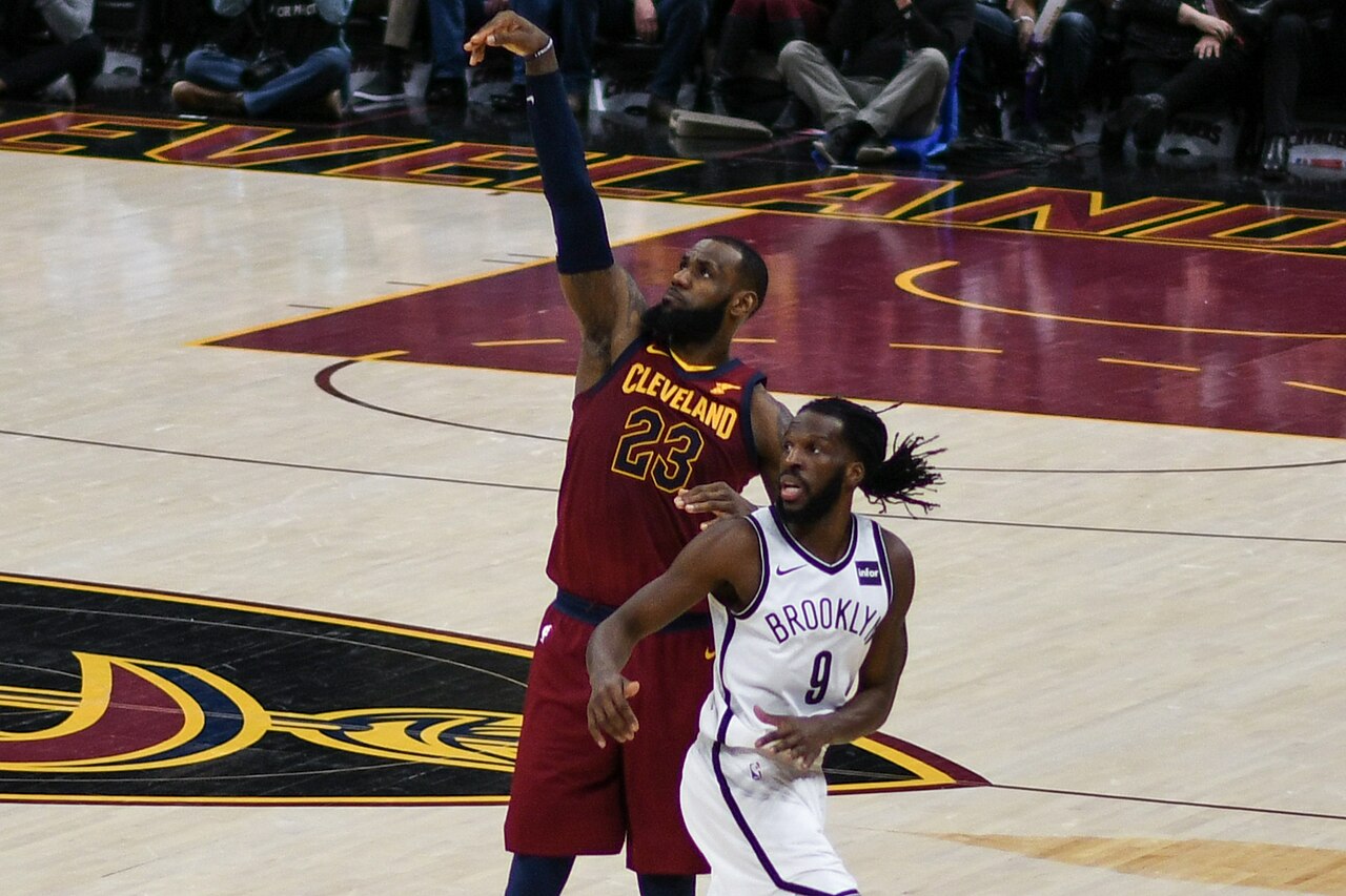 LeBron James in a Cleveland Cavaliers jersey shooting during a game, photographed from courtside at a distance with his head a small part of the frame.