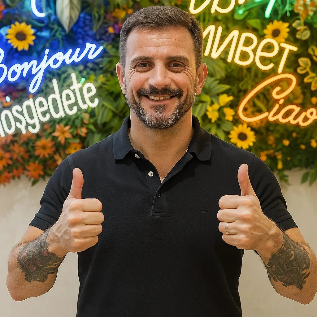 Smiling man giving a thumbs up in front of a colorful floral wall with welcoming signs.